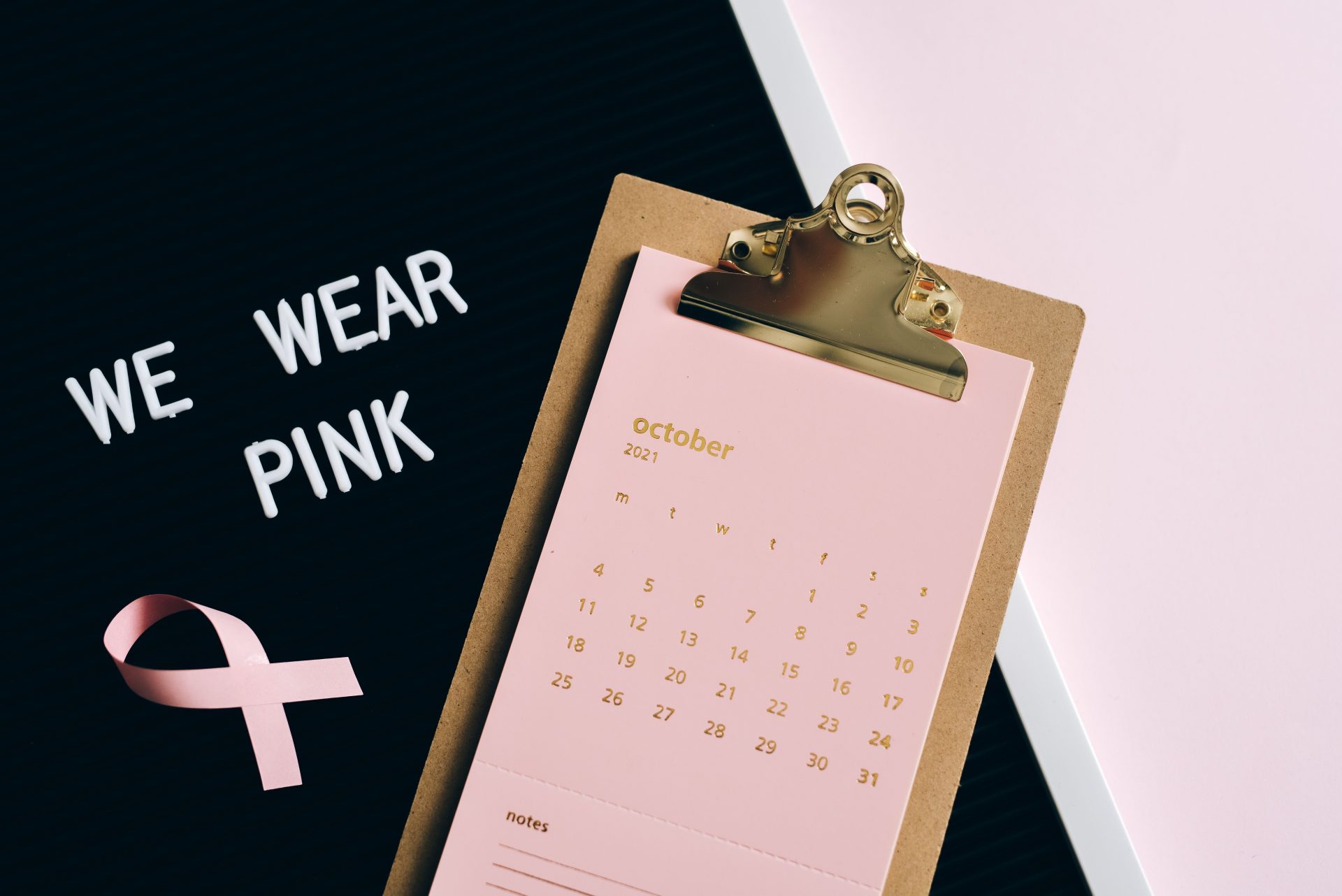 Flat lay image of calendar and pink ribbon for breast cancer awareness in October.